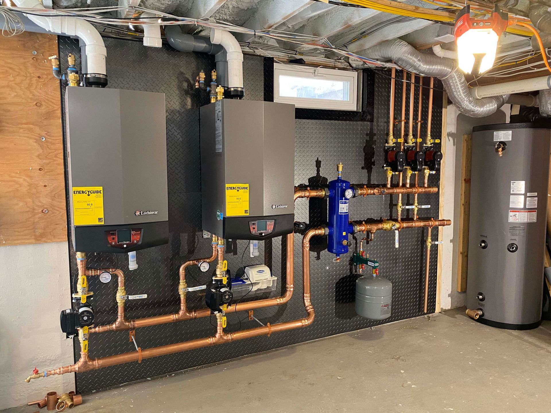 A boiler is sitting in a basement next to a water heater.