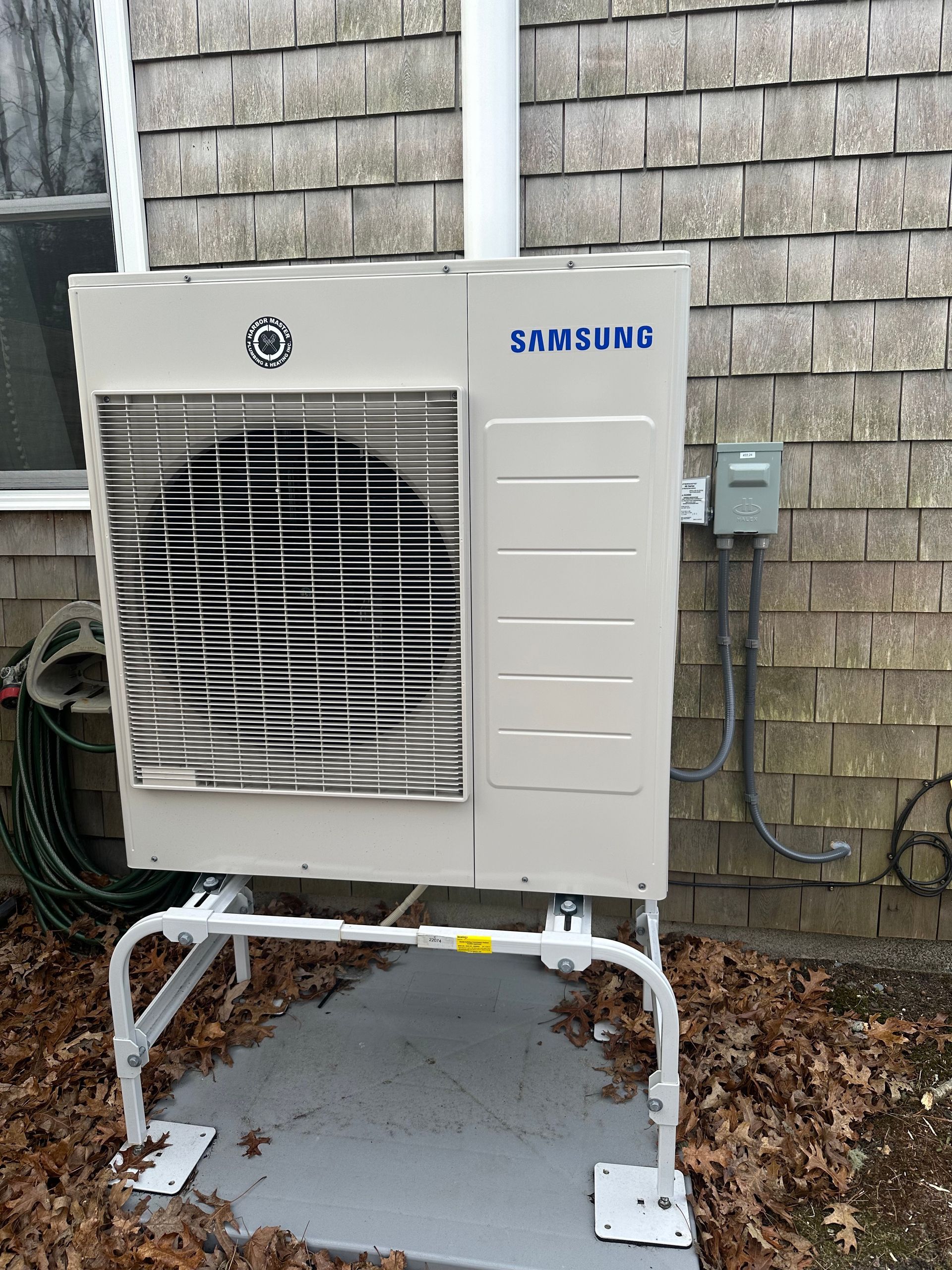 A samsung air conditioner is sitting outside of a house.