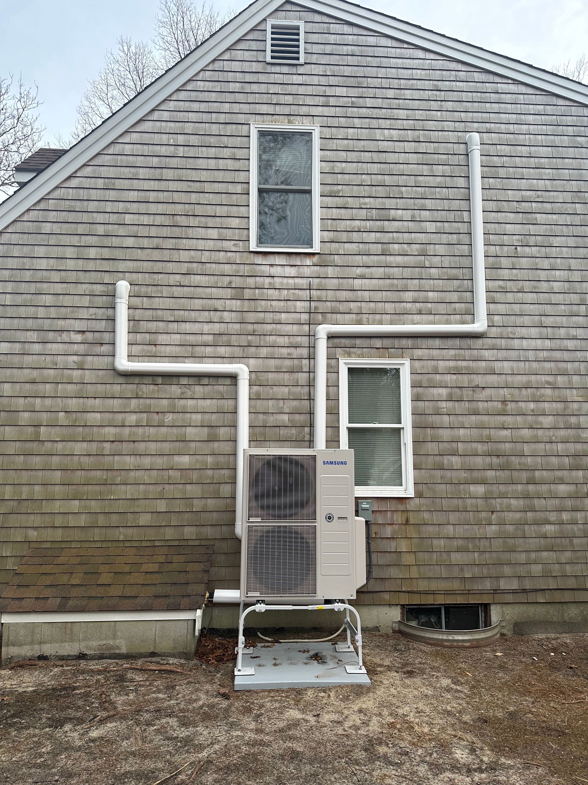 A gray brick house with a white pipe coming out of the side of it.