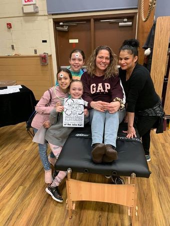 Five smiling people sit and stand around a treatment table in a gym, holding a certificate.