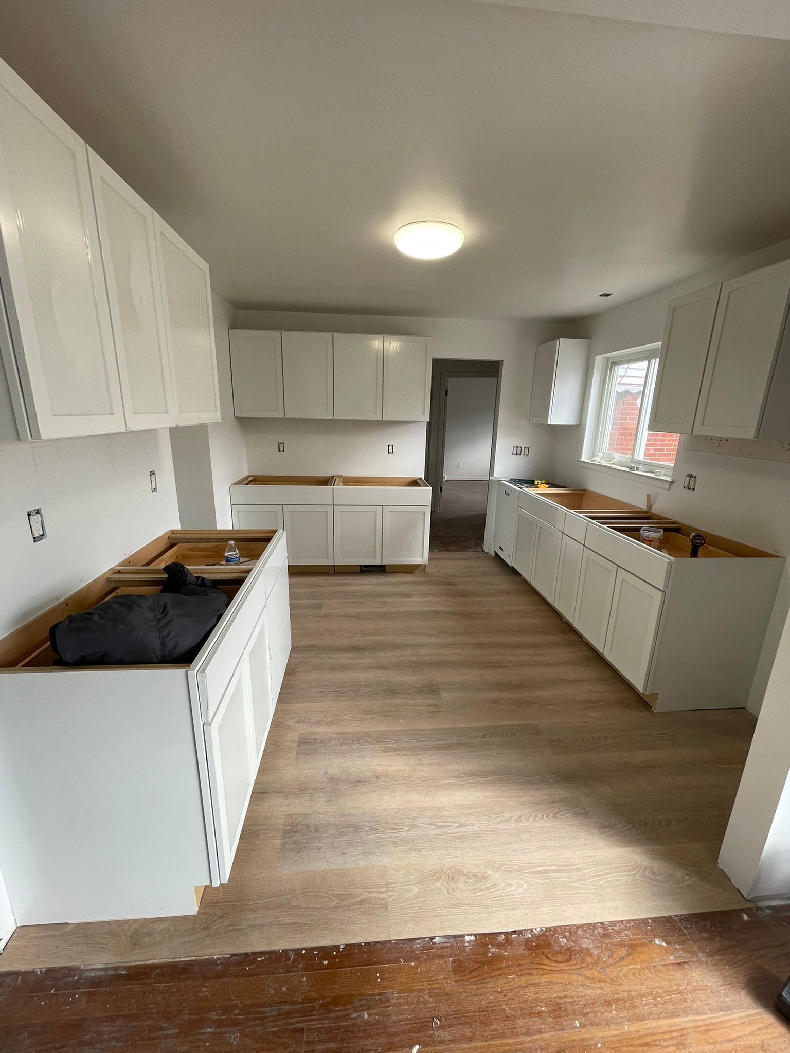 White kitchen cabinets installed in a room with light-colored flooring; construction in progress.