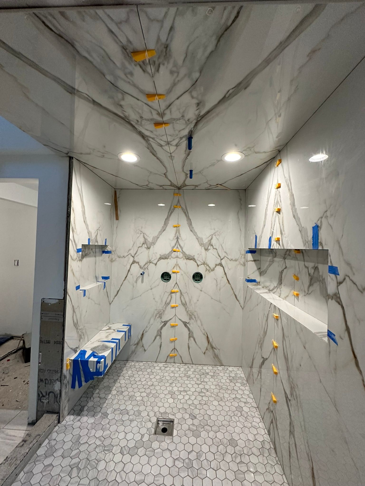Bathroom under construction with white marble tile, shower, and shelves; spacers visible.
