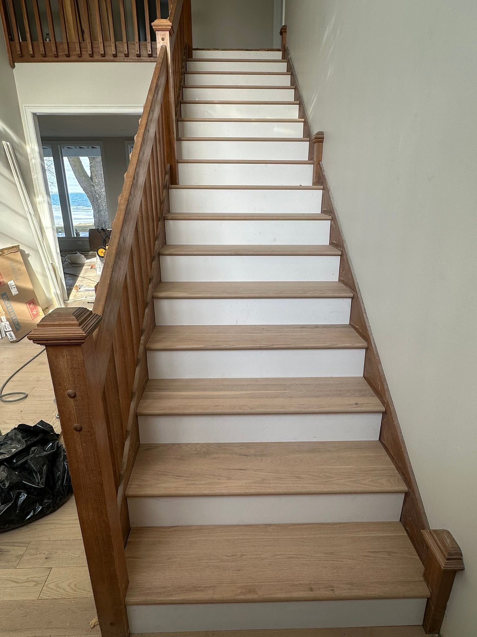 Wooden staircase with light-colored steps and a dark brown banister; construction setting.