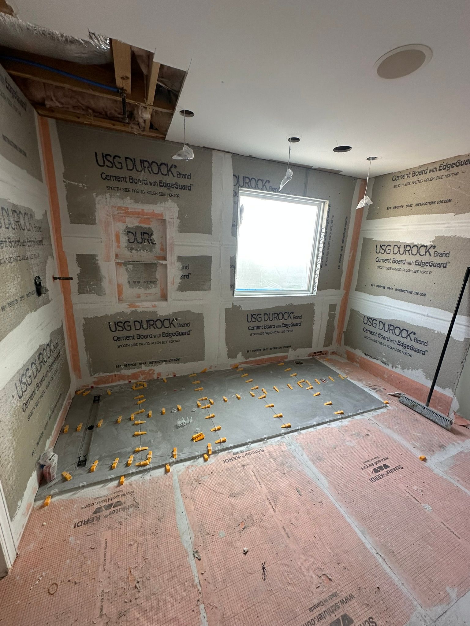Bathroom under construction, with cement board walls, pink underlayment, and a window.