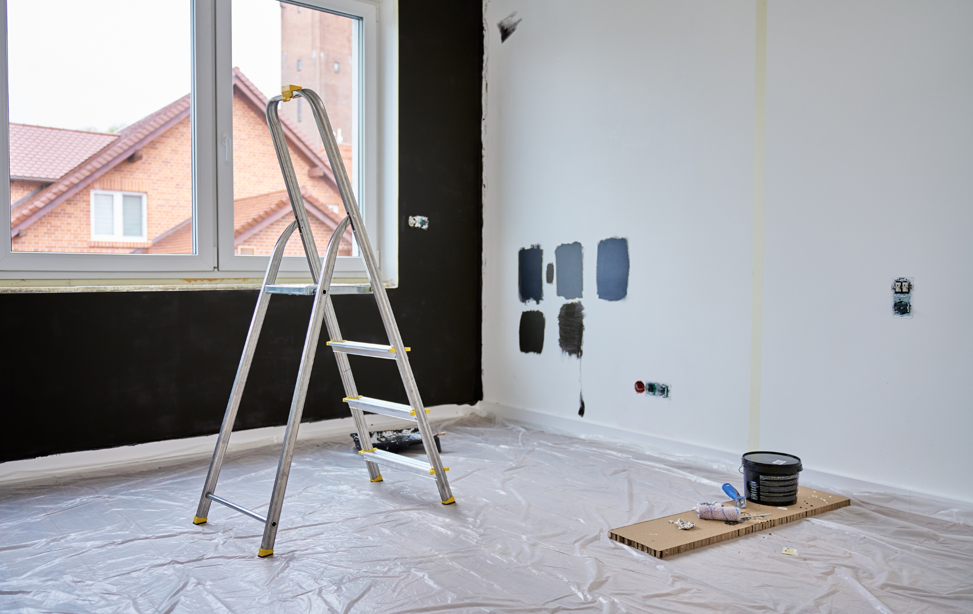 Room with partially painted walls, ladder, paint samples, and paint can on a wooden board.