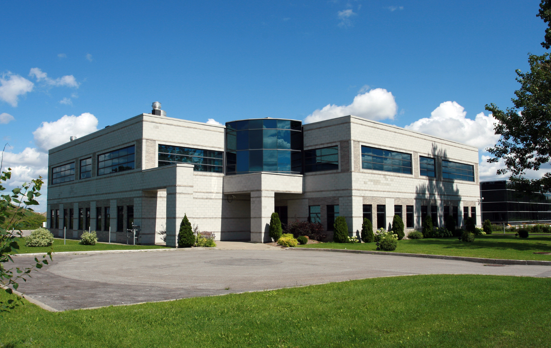 Two-story modern building with blue glass entrance, rectangular windows, and a green lawn.
