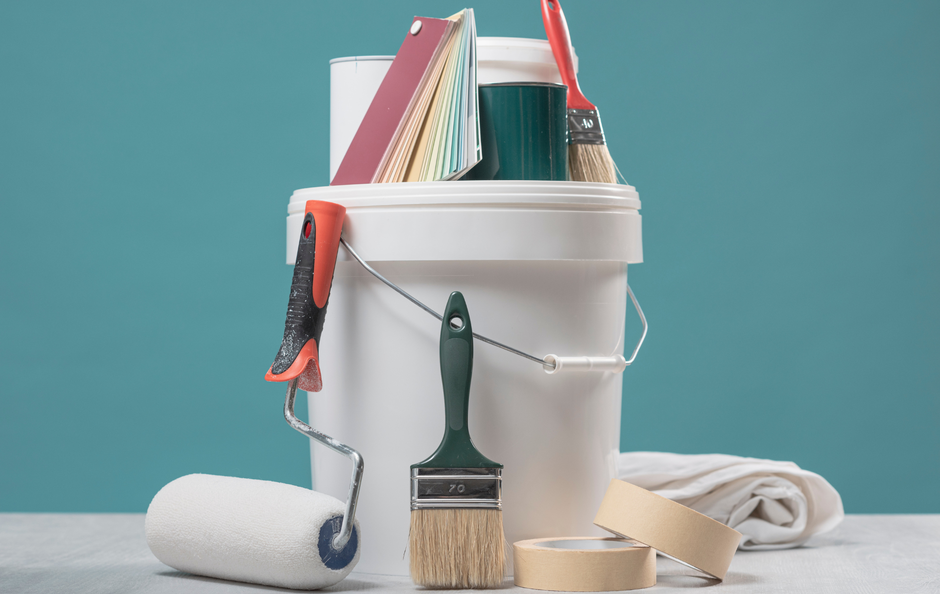 White paint bucket with painting supplies: roller, brushes, tape, and color swatches on a blue background.