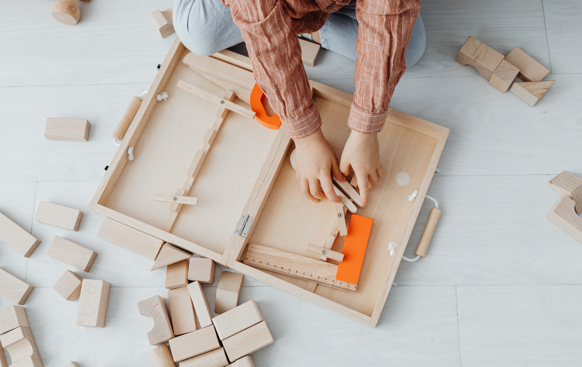 Child playing with wooden blocks and a wooden box on a light-colored floor.