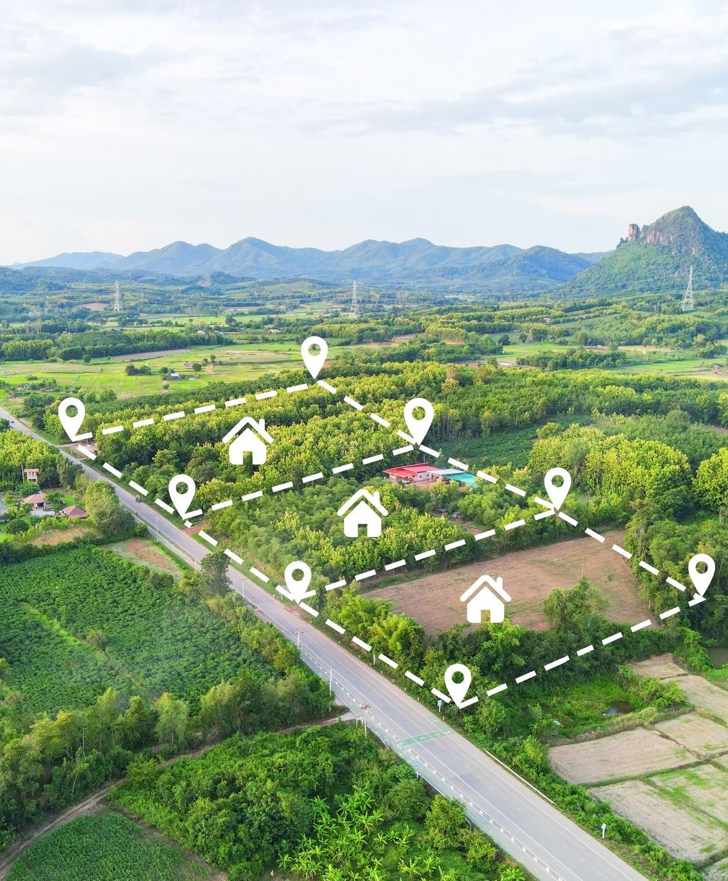 An aerial view of a lush green field with houses and mountains in the background.