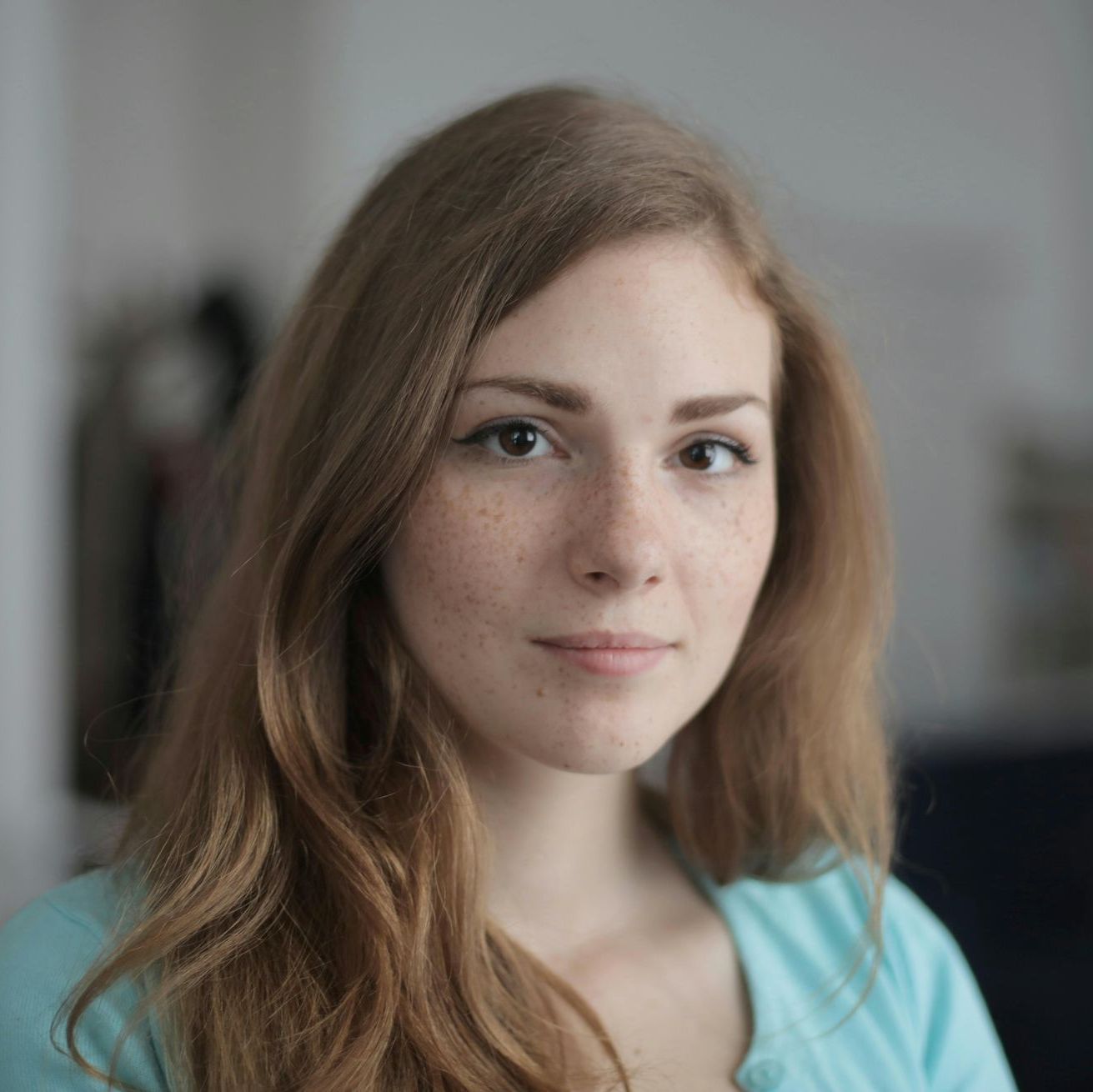 A woman with long brown hair and freckles is wearing a blue shirt and looking at the camera.