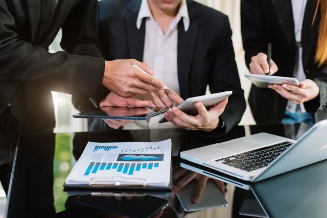 A group of business people are sitting at a table looking at a tablet.