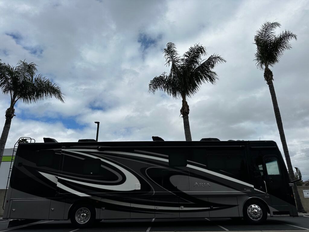 A large rv is parked next to palm trees in a parking lot.