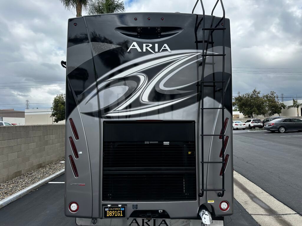 The back of a rv with a ladder attached to it is parked in a parking lot.