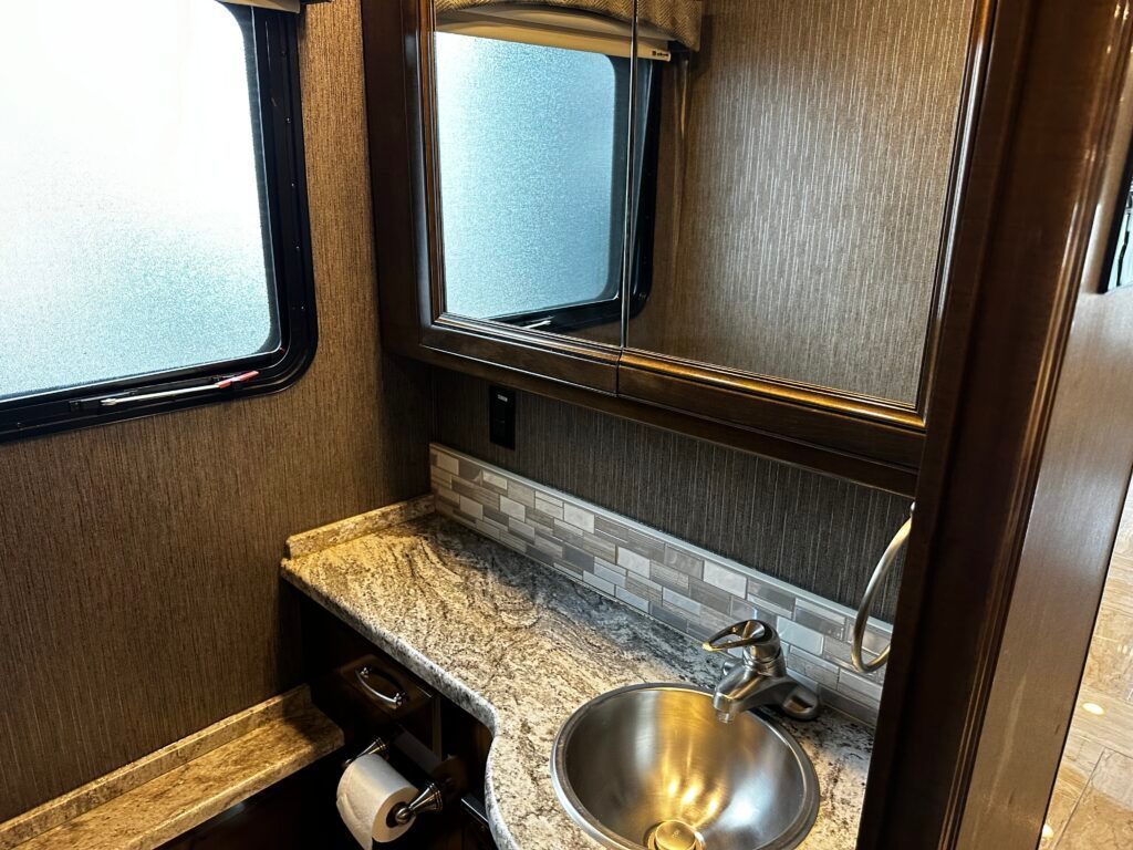 A bathroom with a sink , mirror and toilet paper.