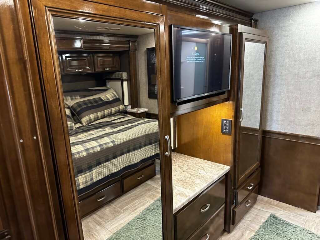 A bedroom in a rv with a bed and a flat screen tv.