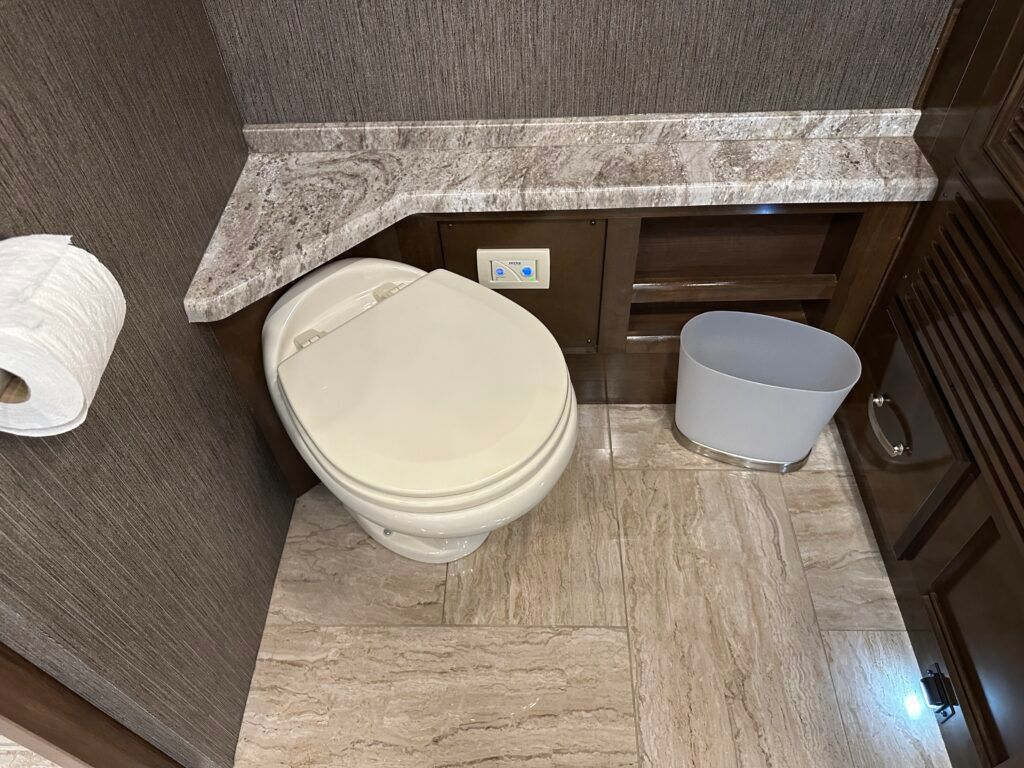 A bathroom with a toilet , trash can and toilet paper.