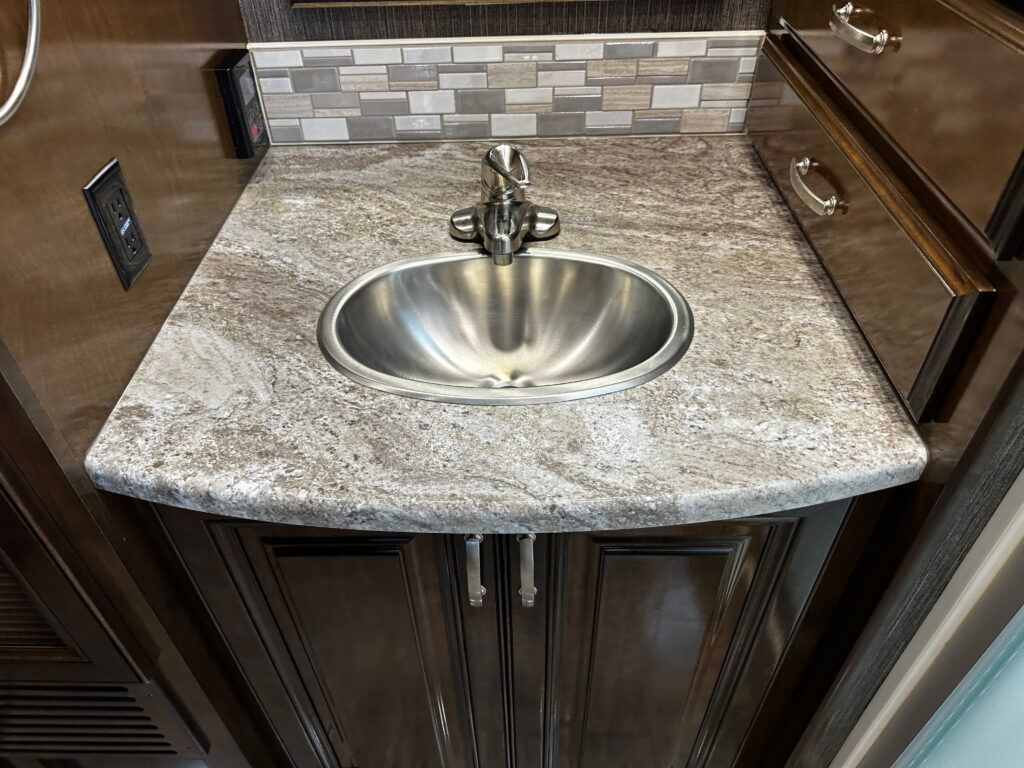 A bathroom sink with a granite counter top and a stainless steel sink.