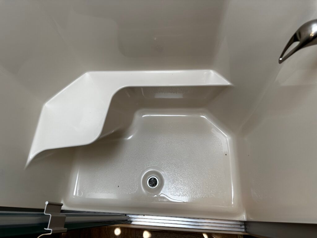 A shower stall with a seat and a drain in a bathroom.