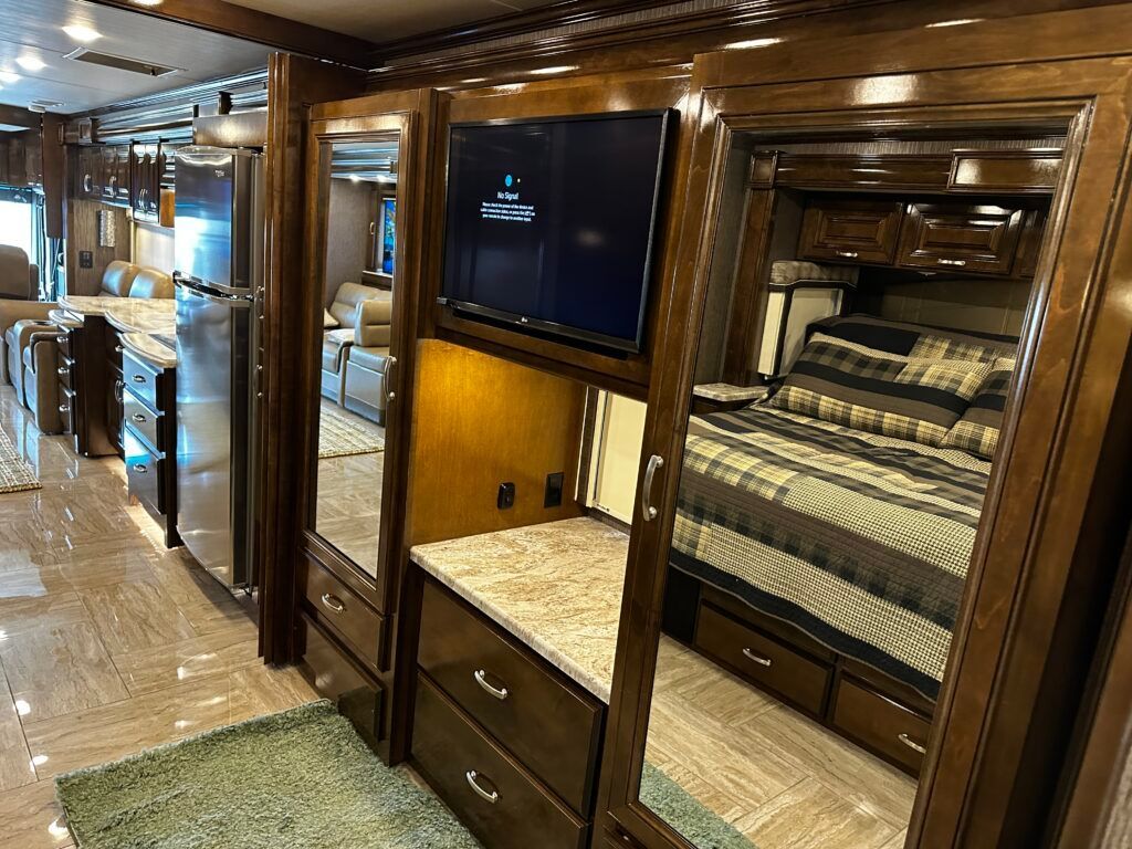 A bedroom in a rv with a bed , television , and mirrors.