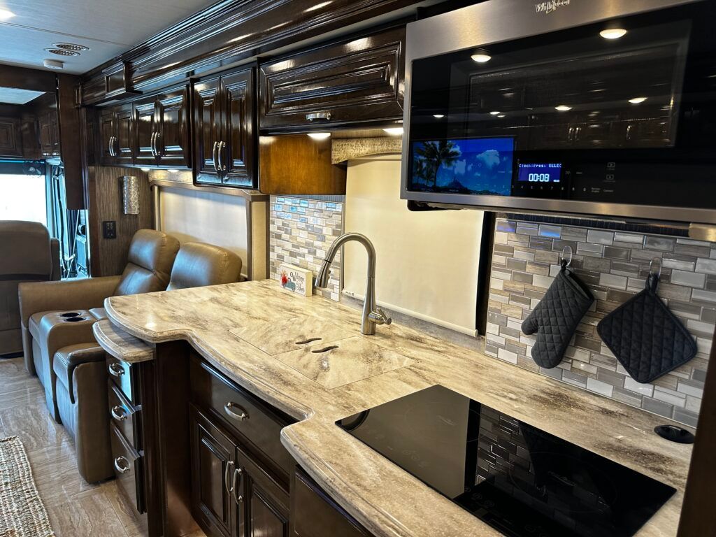 A kitchen in a rv with a sink , stove , microwave and television.