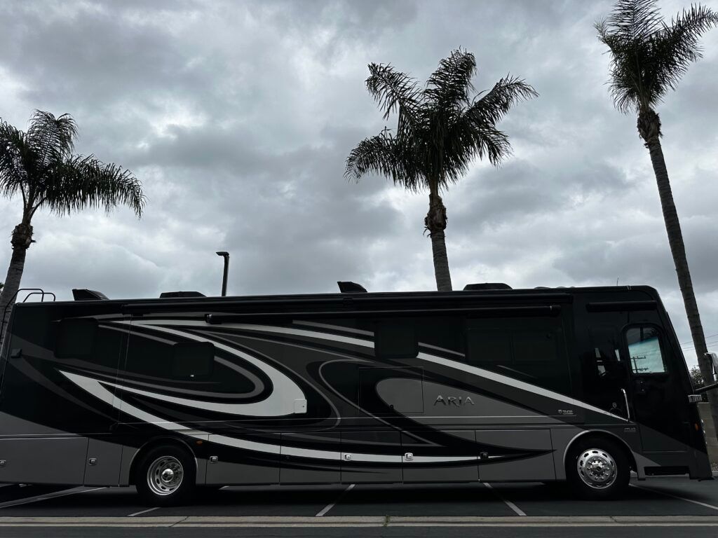 A large rv is parked in a parking lot next to palm trees.