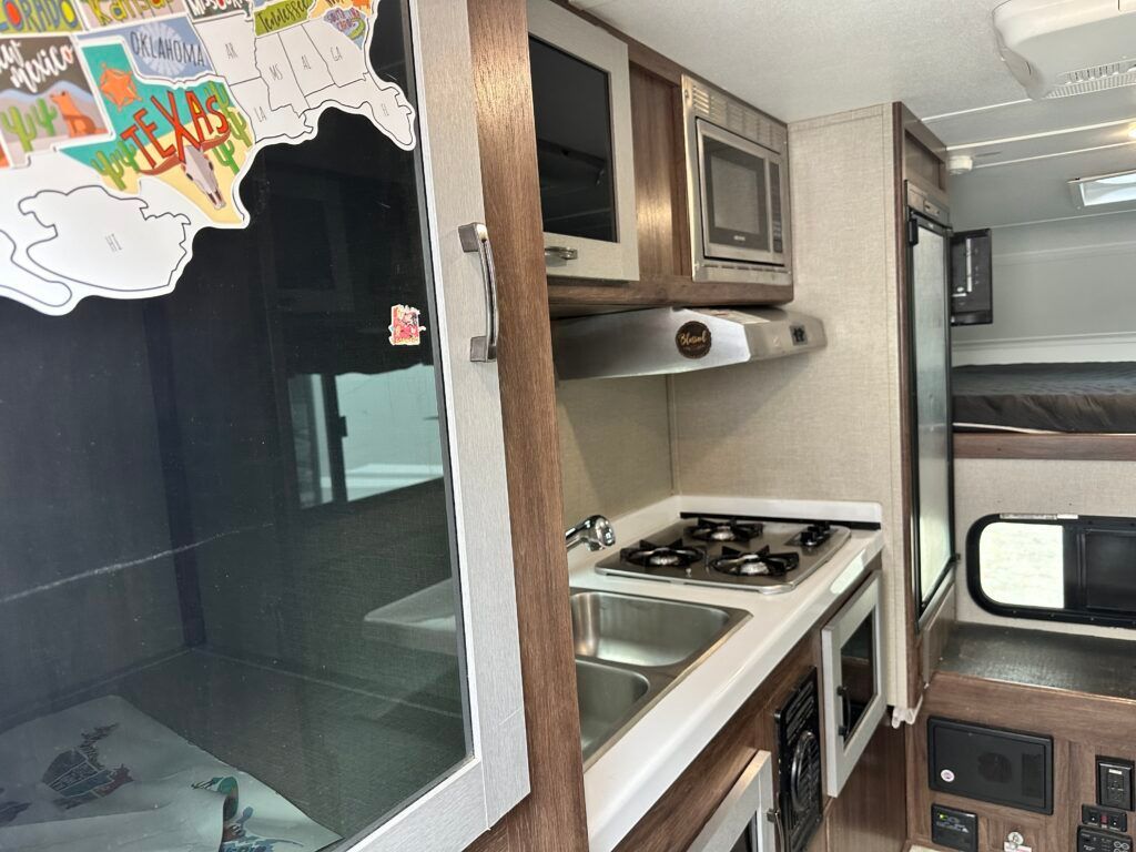 A kitchen in a rv with a sink , stove , microwave and a map of the united states