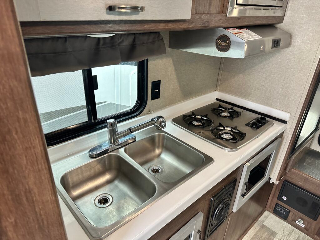 A kitchen in a rv with a sink , stove and microwave.