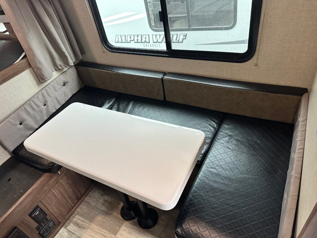 A white table is sitting on top of a black couch in a rv.