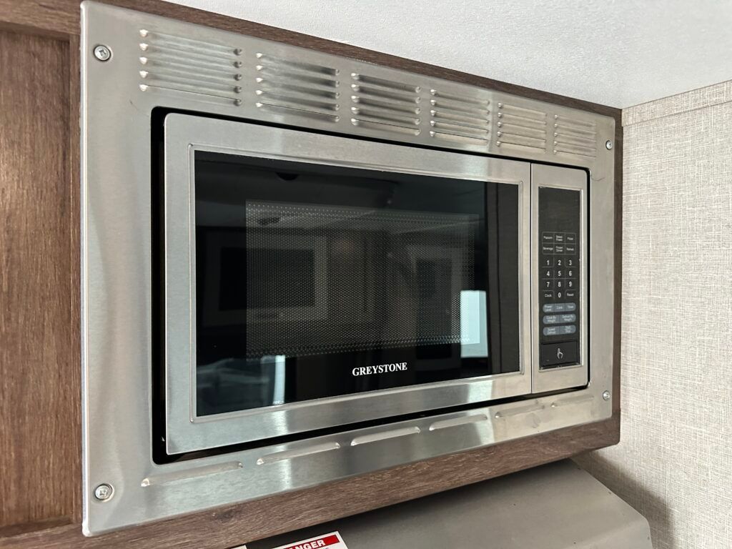 A stainless steel microwave oven is built into a wooden cabinet.