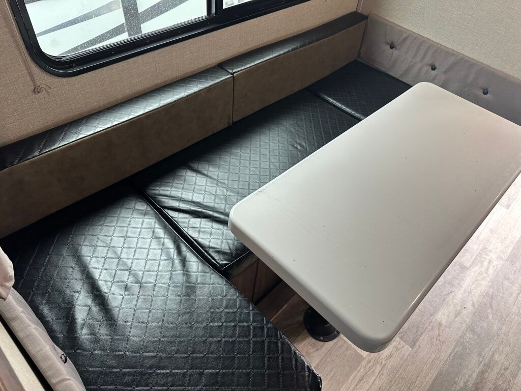 A white table is sitting on top of a black couch in a camper.