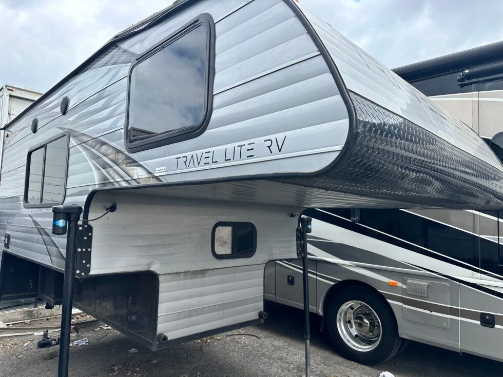 A travel lite rv is parked next to a bus.