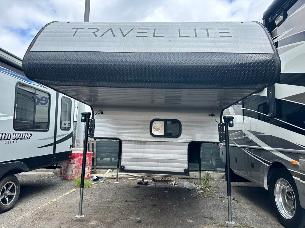 A travel lite trailer is parked next to a rv in a parking lot.