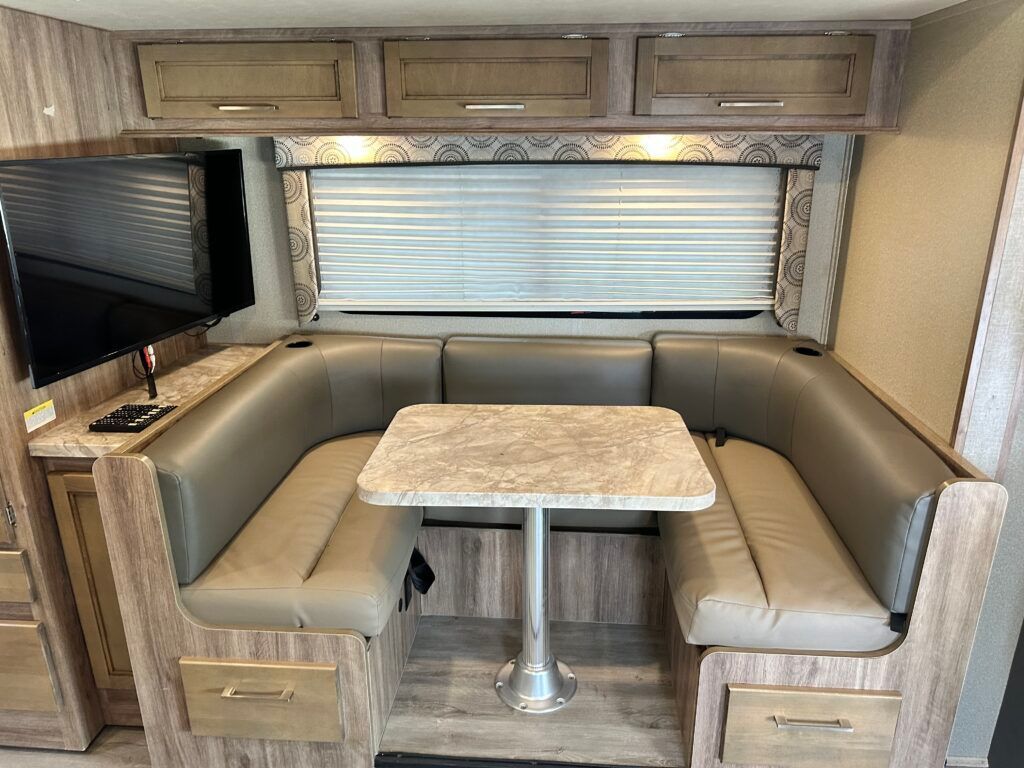 A rv with a table , benches , and a flat screen tv.