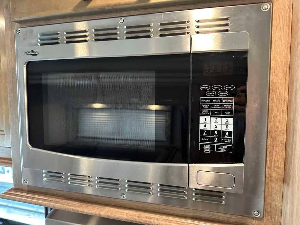 A stainless steel microwave oven is built into a wooden cabinet.
