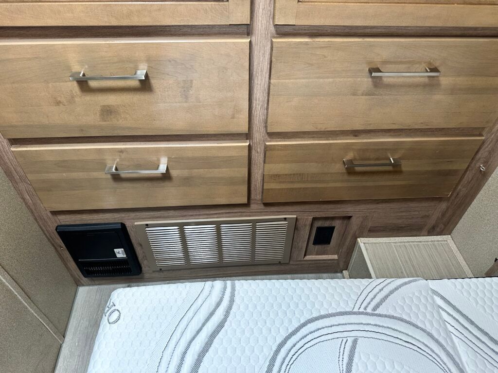 A bedroom with a mattress , drawers , and a fan.
