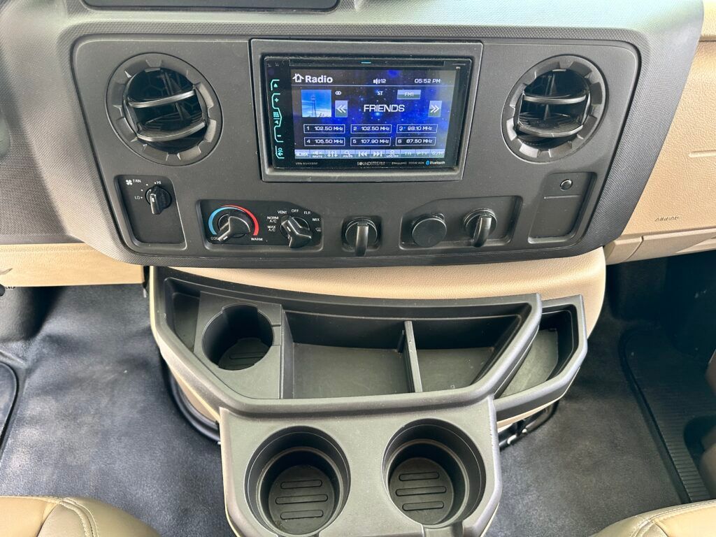 The dashboard of a van with a radio and cup holders