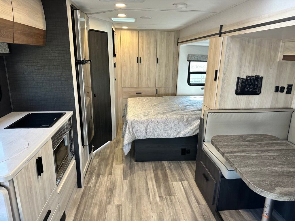 The inside of a rv with a bed , table , and kitchen.