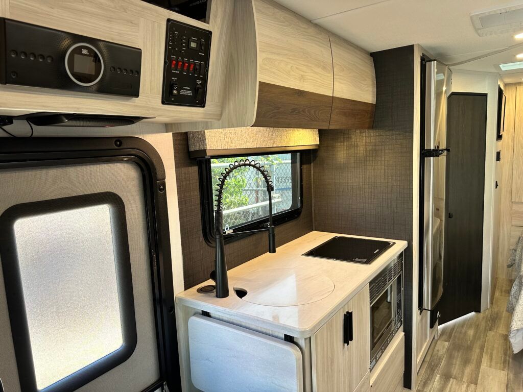 A kitchen in a rv with a sink , stove , refrigerator and microwave.