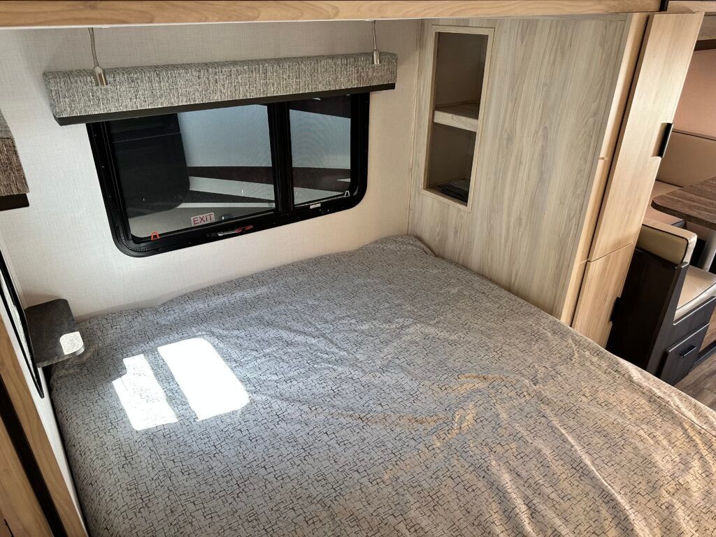 A bedroom in a rv with a bed and a window.