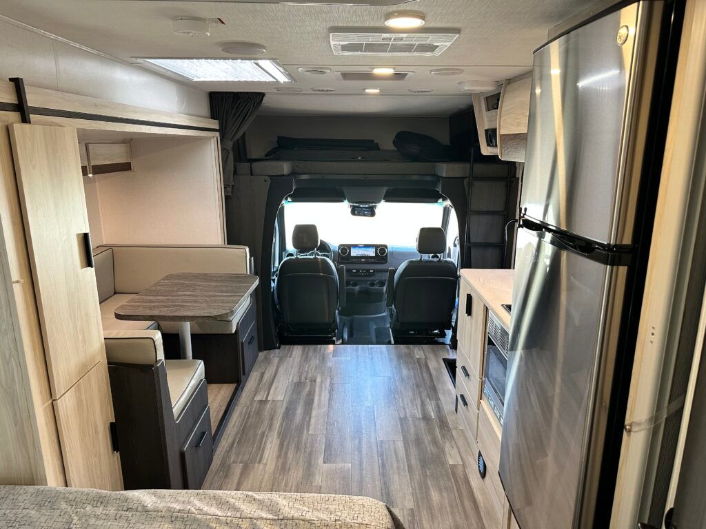 The inside of a rv with a bed , table , and refrigerator.