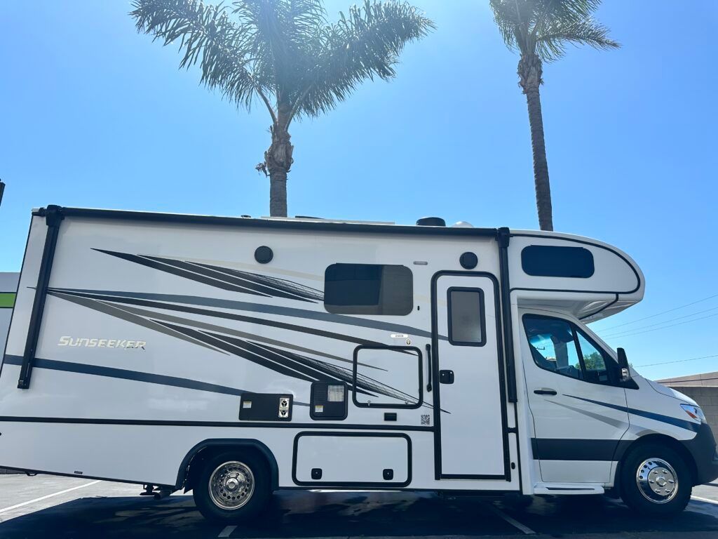 A white rv is parked in a parking lot next to palm trees.