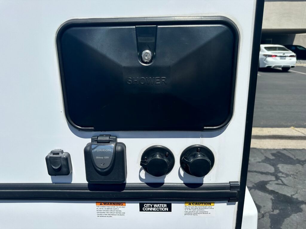 A white rv with a black door and electrical outlets on the side.