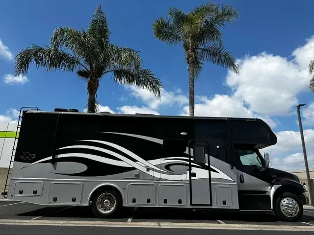 A black and white rv is parked in a parking lot next to palm trees.