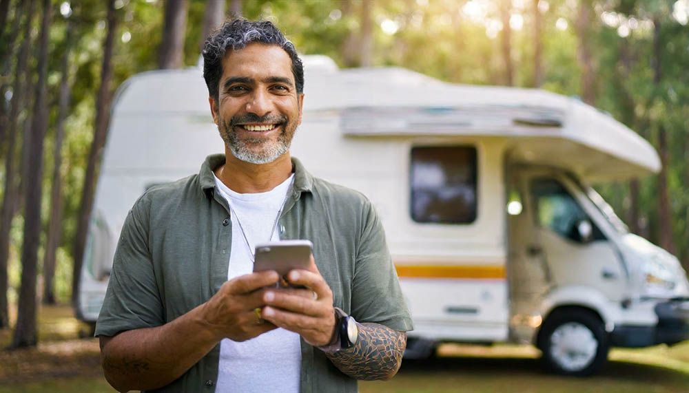 A man is holding a cell phone in front of a camper van.