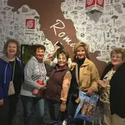 Five people smiling in front of a patterned wall with the word “Roma” and a shop logo.