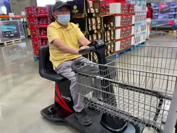 A man wearing a mask is riding a shopping cart in a store