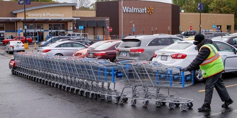 A man is pushing a stack of shopping carts in a parking lot.