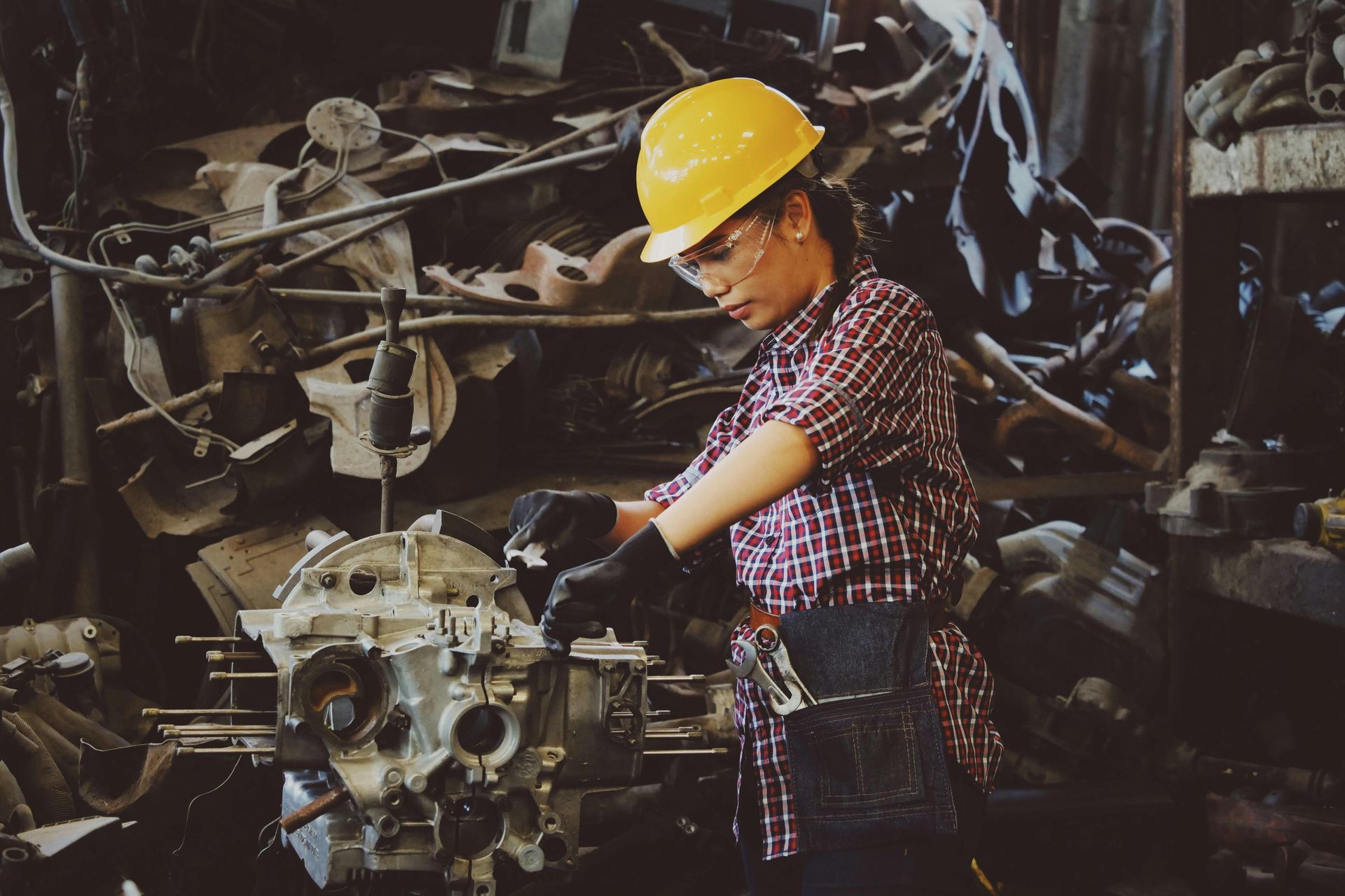 A man wearing a hard hat and safety glasses is working on a machine in a factory.