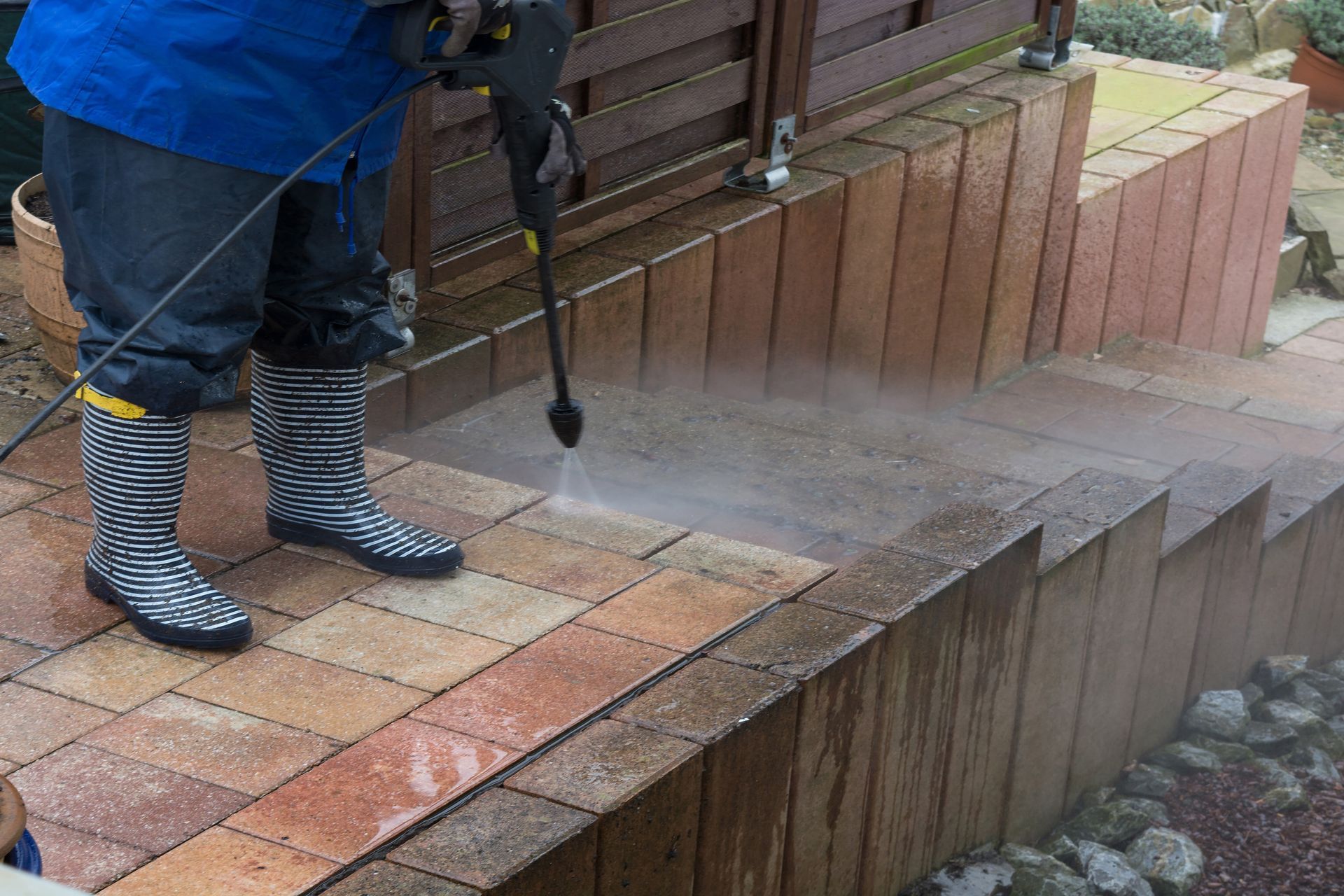 A person is using a high pressure washer to clean a brick walkway.