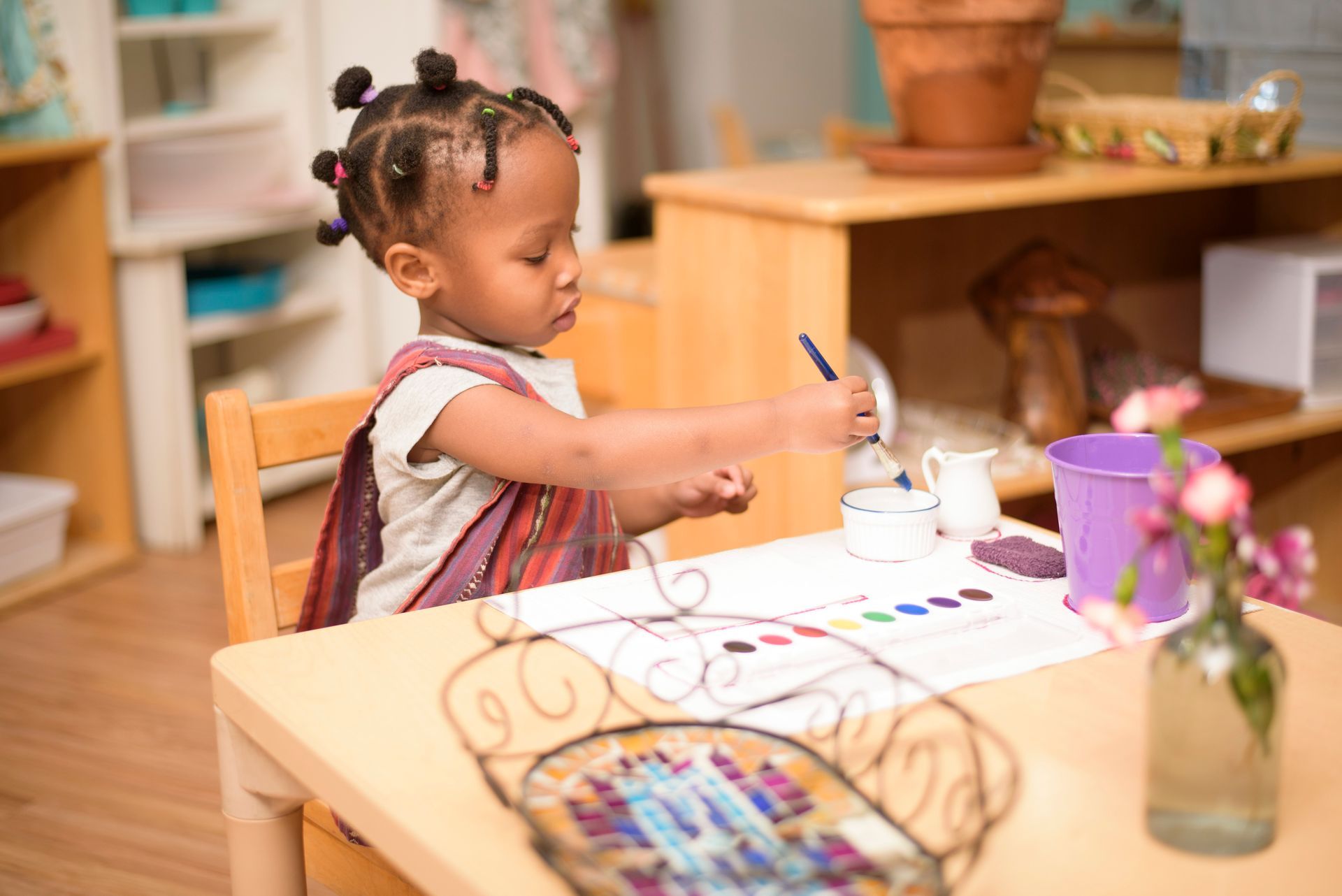 a Montessori  little girl is sitting at a table painting with a brush .